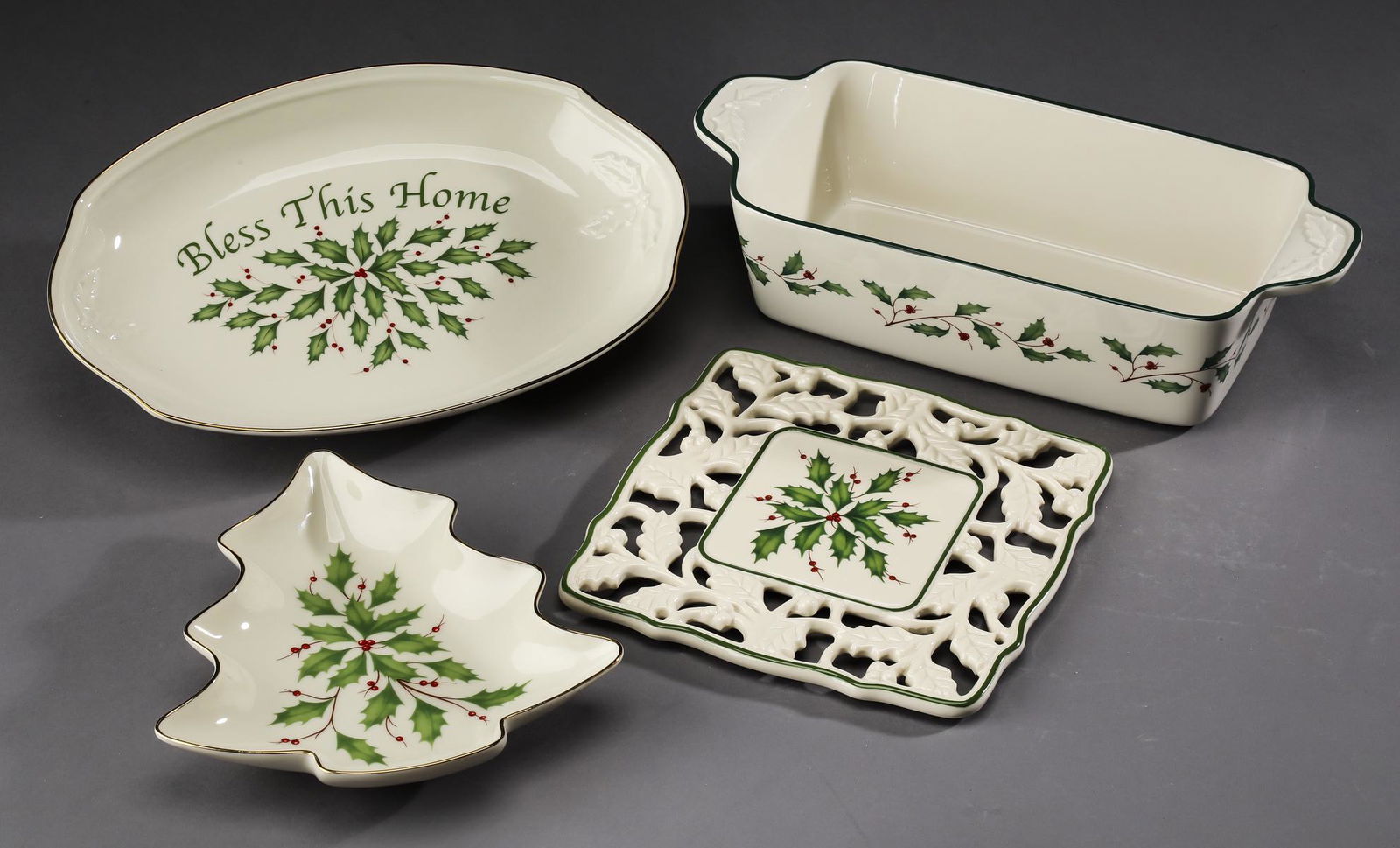 (4) Lenox porcelain table accessories in 'Holiday': Lenox porcelain table accessories in the 'Holiday' pattern, including: (1) tree shaped dish; (1) loaf pan; (1) 'Bless this House' oval tray; and (1) trivet; each decorated in a holly leaf motif accent
