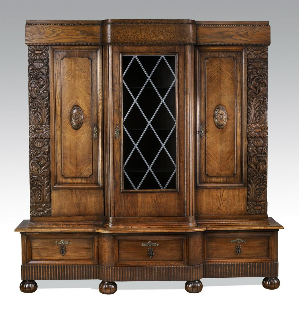 Art Deco oak bookcase, ca 1930, 80"h: Art Deco oak bookcase, likely English, circa 1930, having a stepped molded cornice above a glazed door opening to three glass shelves, flanked by doors with a relief carved foliate stripe next to a pa