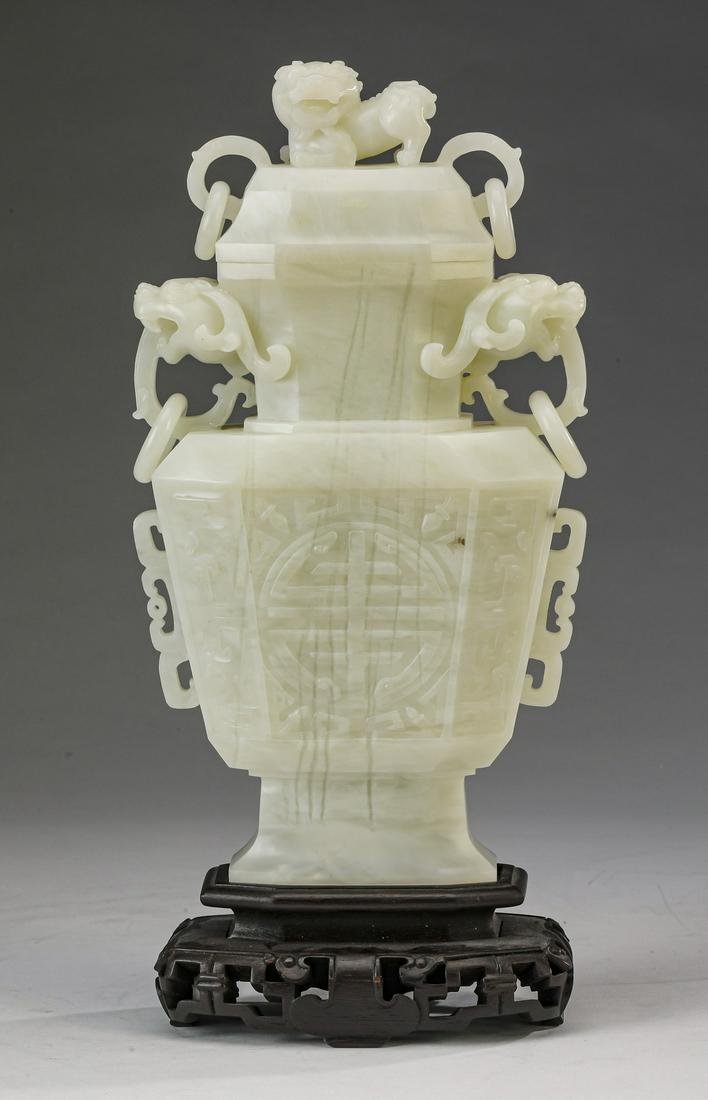 Chinese white jade covered urn with Fu lion, 13"h: Chinese carved white jade covered urn, of faceted baluster form, having a Fu lion finial flanked by loose rings, above a faceted and domed lid, surmounting a tapering neck flanked by dragon mask handl