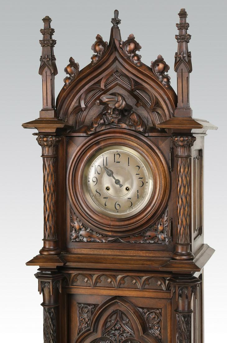 19th c. French Gothic Revival walnut tall case clock: 19th c. French Gothic Revival walnut tall case clock, having a Gothic arched pediment centering a bust of a bearded man in a medieval feathered hat flanked by buttress finials, over a circular brass f