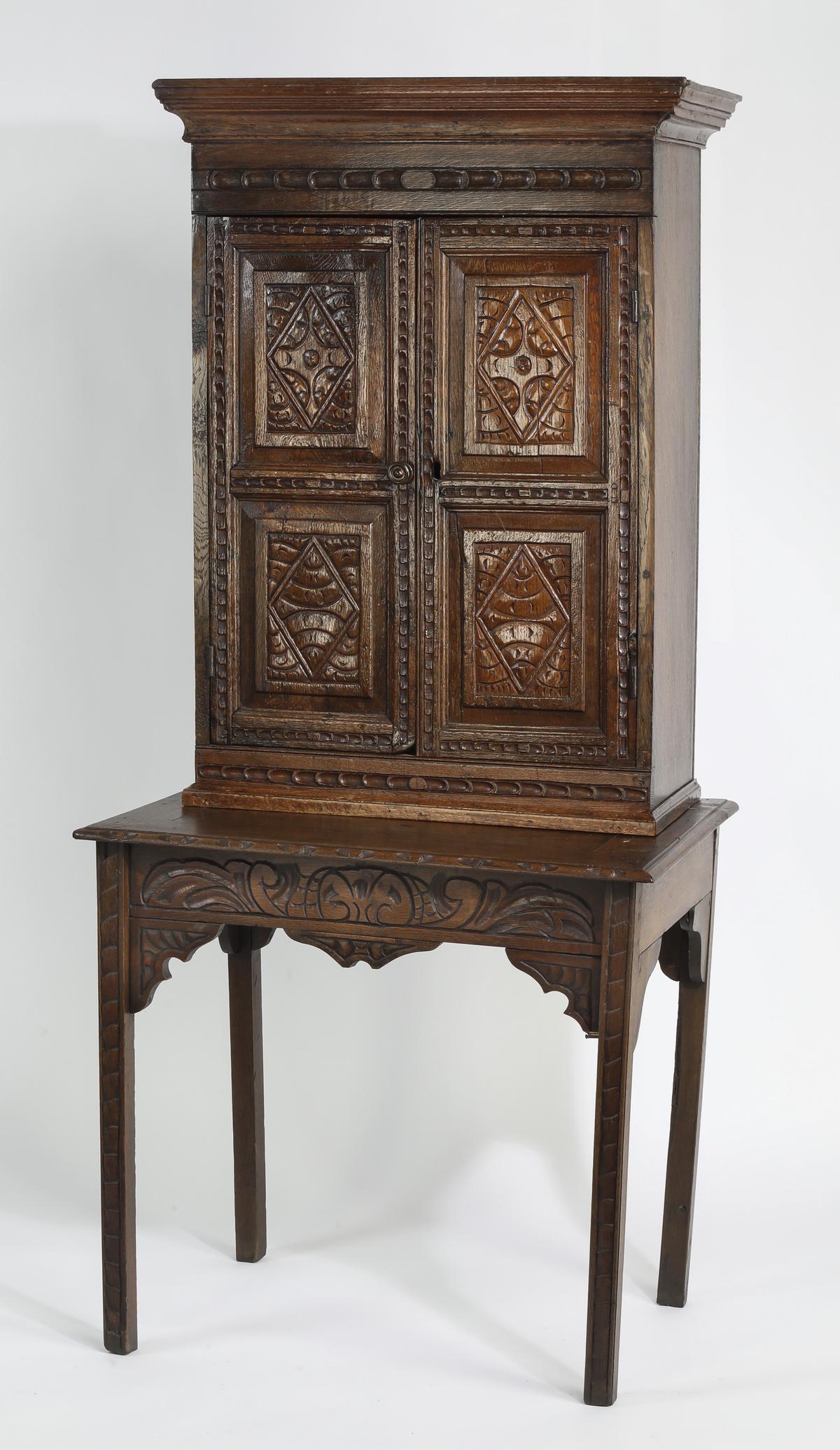 19th c. English carved oak cabinet on stand: 19th c. English carved oak cabinet on table stand, having a stepped cornice above two doors carved with geometric patterns, opening to two shelves, resting on a rectangular table base with a wide carv