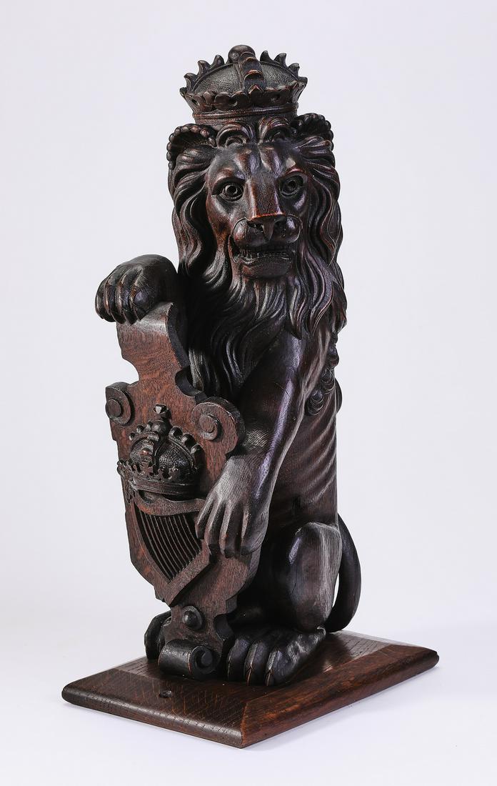 Carved oak architectural element, lion with shield: Carved oak architectural element, early 20th century, depicting an erect seated crowned lion holding an heraldic shield ornamented with a crown and harp, mounted on a rectangular base, 17"h x 9"w x 6"