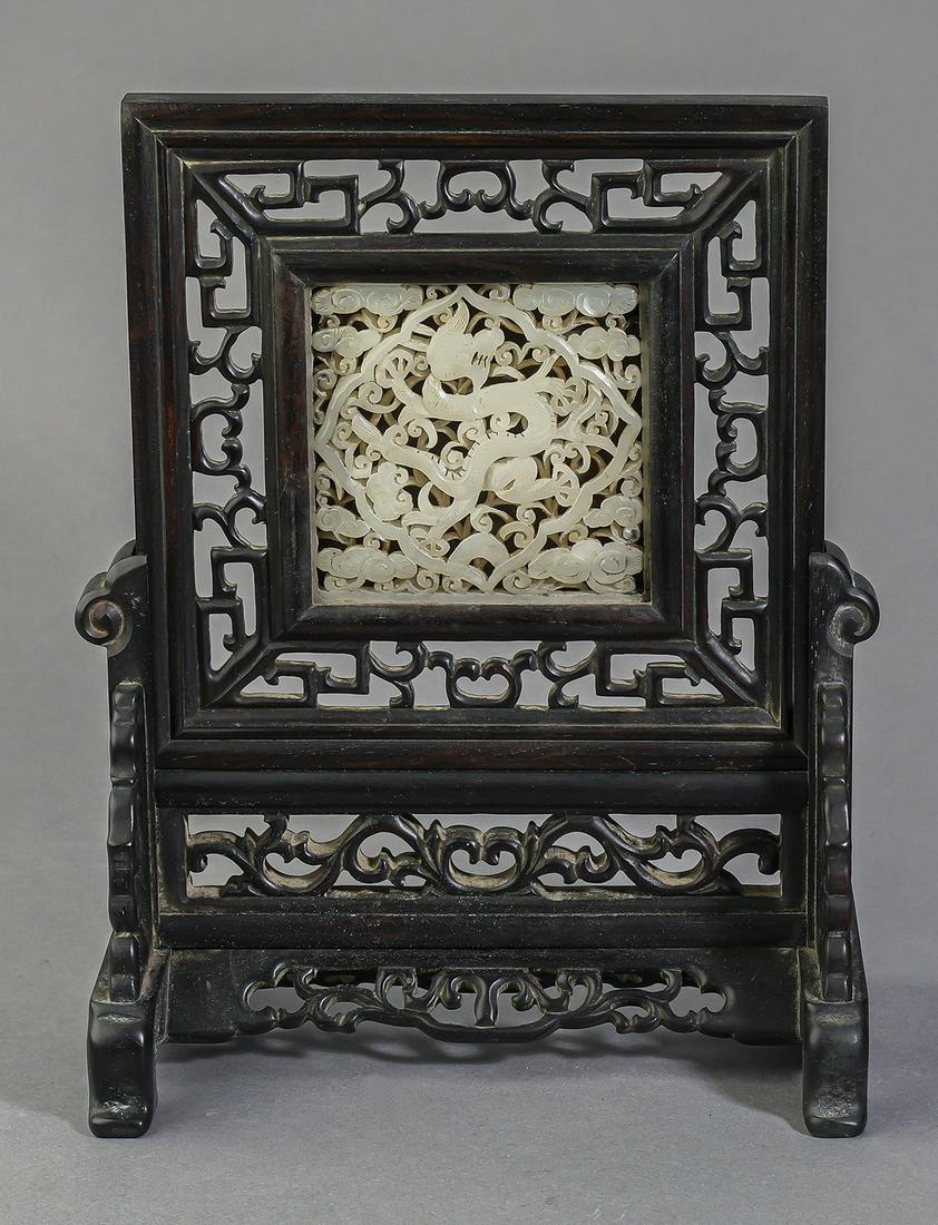 Chinese carved and pierced white jade table screen: Diminutive Chinese carved and pierced white jade table screen, the square jade plaque depicting a writhing dragon within a cartouche surrounded by auspicious cloud forms, framed in wooden fretwork and
