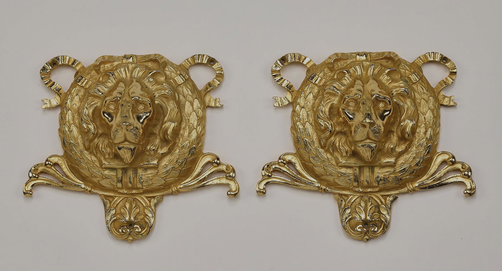Pair of gilt bronze lion mask decorative appliques: Pair of Italian gilt bronze decorative appliques, each in the form of lion masks centered by laurel wreaths and ribbons rising on acanthus scrollwork, 6"h x 7"w x 2"d.