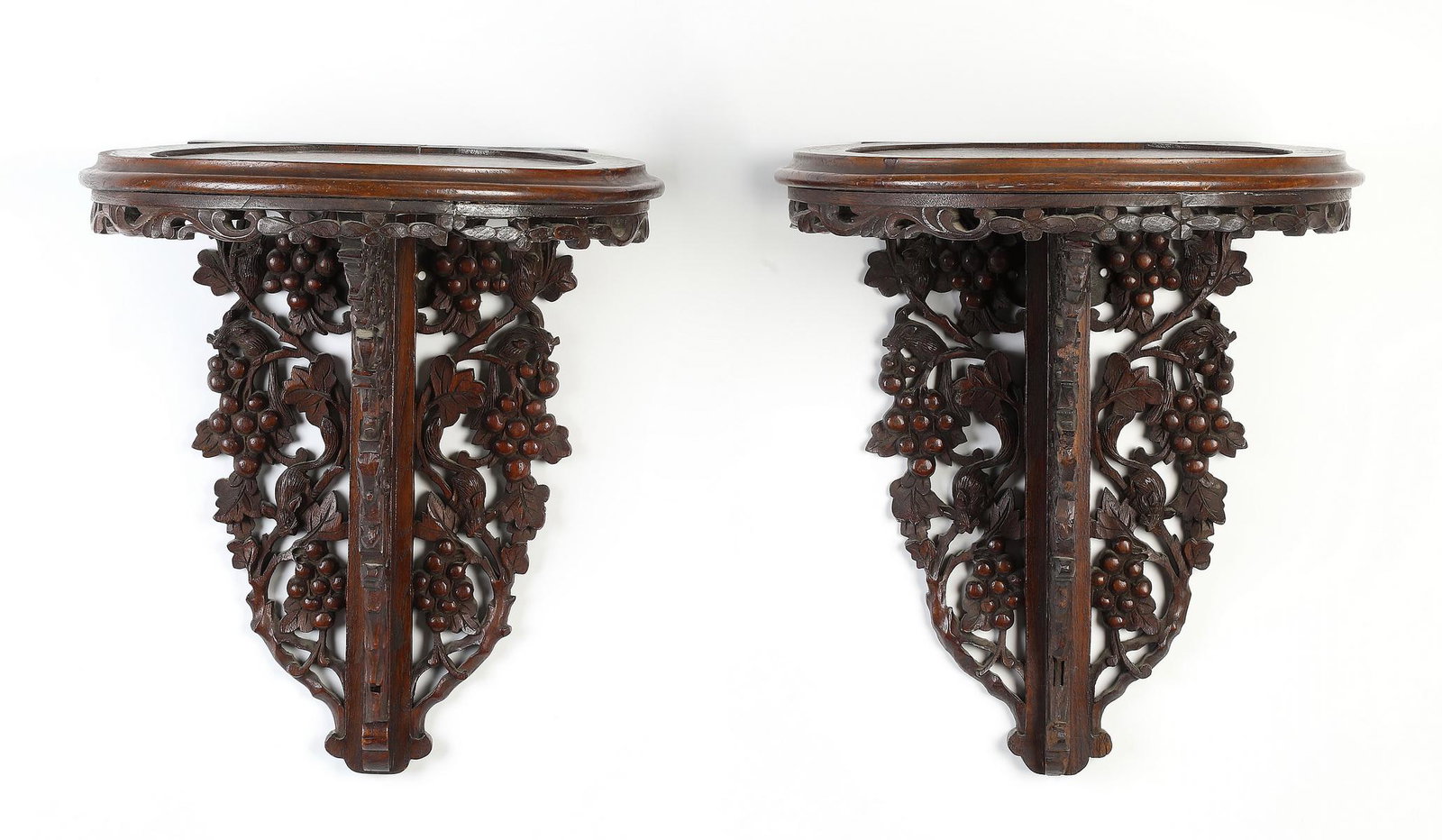 Pair of carved wall brackets w/ grapevines: Pair of carved hardwood wall brackets, having a circular surface with a pierced apron rising on a pierce-carved bracket of flowering vines, connected to a pierce-carved backsplash of mice climbing gra