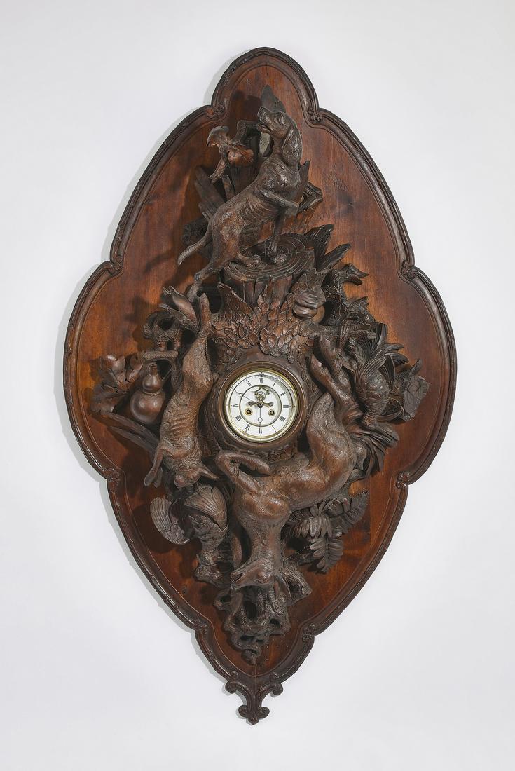 19th c. Black Forest clock with game trophies, 51"h: Black Forest carved oak wall clock, late 19th century, of navette form, ornamented with a hound, a rabbit, a chamois goat, and a game bird arranged around a circular clock having a white face and Roma