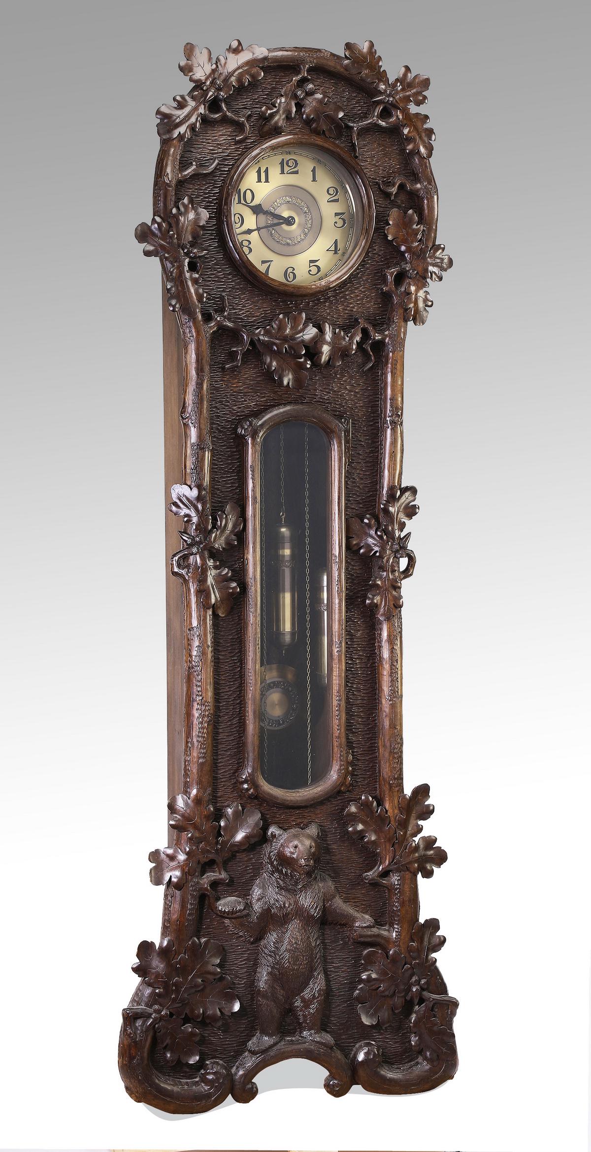 German Black Forest tall case clock w/ bear, 83"h: German Black Forest tall case clock, circa 1925, the highly carved case having a naturalistic arched crest framed by carved oak leaves and acorns, above a brass dial with Arabic numerals, surmounting 