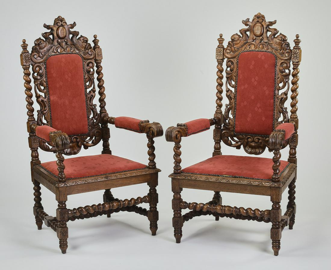 (2) 19th c. Jacobean style carved oak throne chairs: Pair of Jacobean style throne chairs, late 19th or early 20th century, executed in carved oak, having a cabochan medallion flanked by dolphin figurals rising on the upholstered back accented with hail