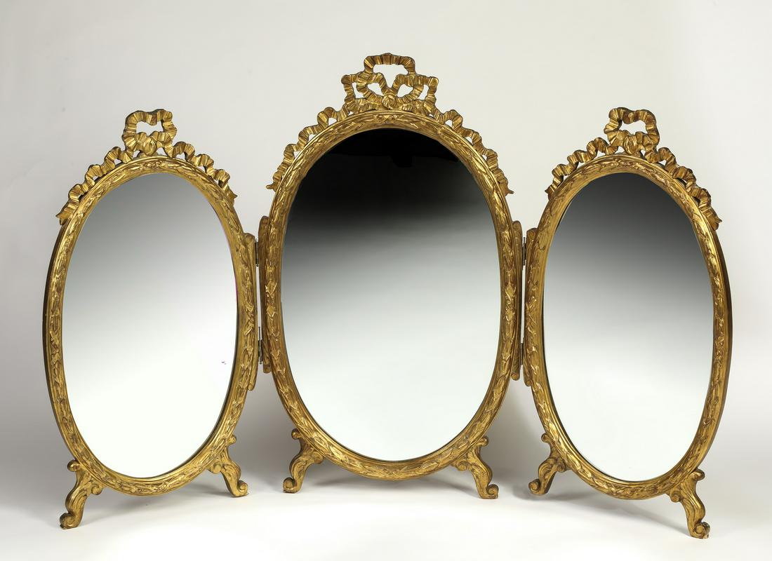 Continental Rococo style giltwood vanity mirror, 63"w: Continental Rococo style giltwood vanity mirror, having oval triptych mirrors, each with a carved bow and garland crest, resting on acanthus C-scroll feet, 40.5"h x 63"w.