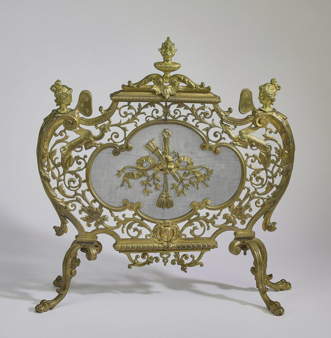 19th c. Louis XV style gilt brass fire screen: Louis XV style gilt brass fire screen, late 19th century, having a flaming urn finial, above a scrolling foliate frame with winged term figures, centering an archery trophy against a mesh screen in a 