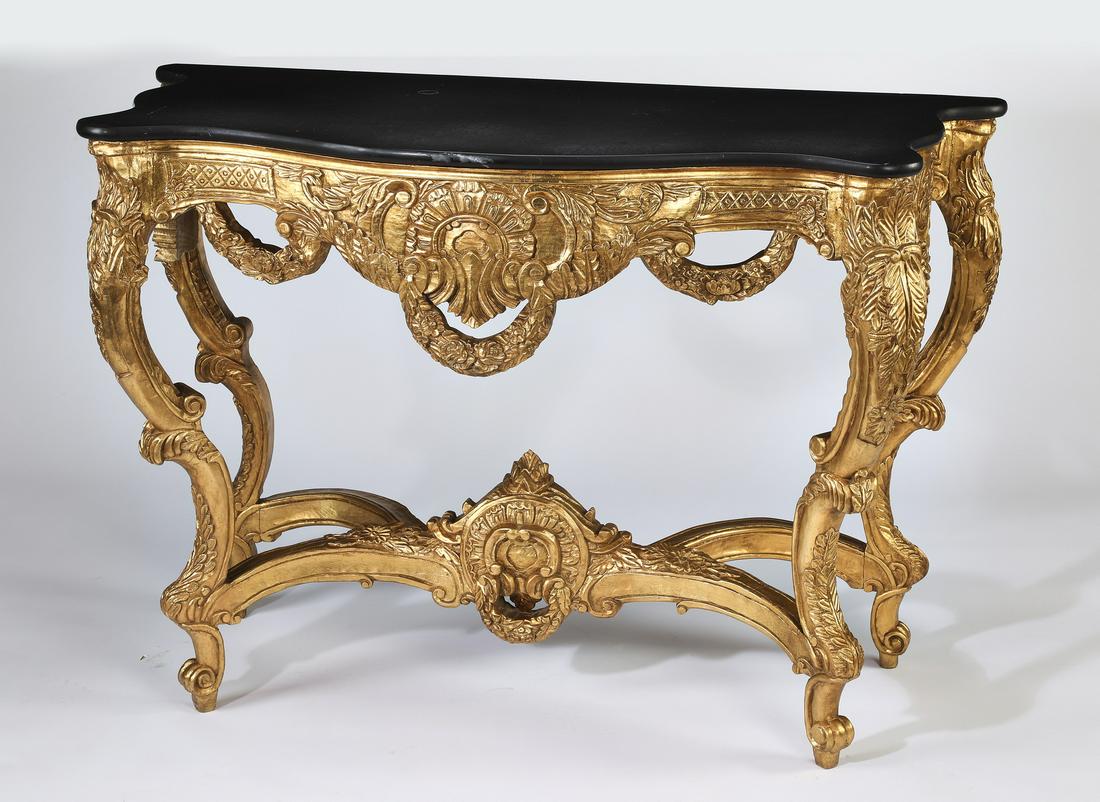 Louis XV style black marble and gilt console table: Black marble and gilt wood console table in the Louis XV taste, having a serpentine top over a pierced and carved apron decorated with shells and swags, rising on acanthus ornamented cabriole legs ter