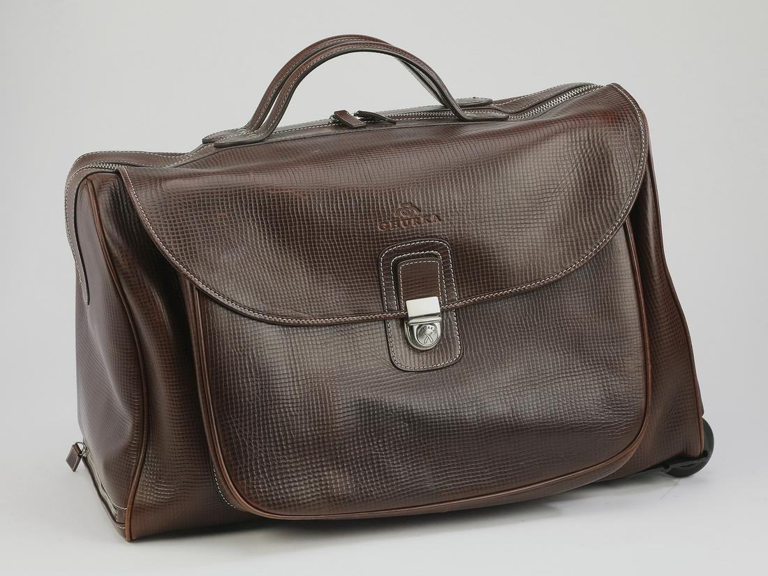 Ghurka leather wheeled overnight bag, 19"l: Ghurka wheeled overnight bag, executed in textured walnut leather, having a front snap flap opening to a pocket, with a main compartment having a large zippered pocket on one side and and small fitted