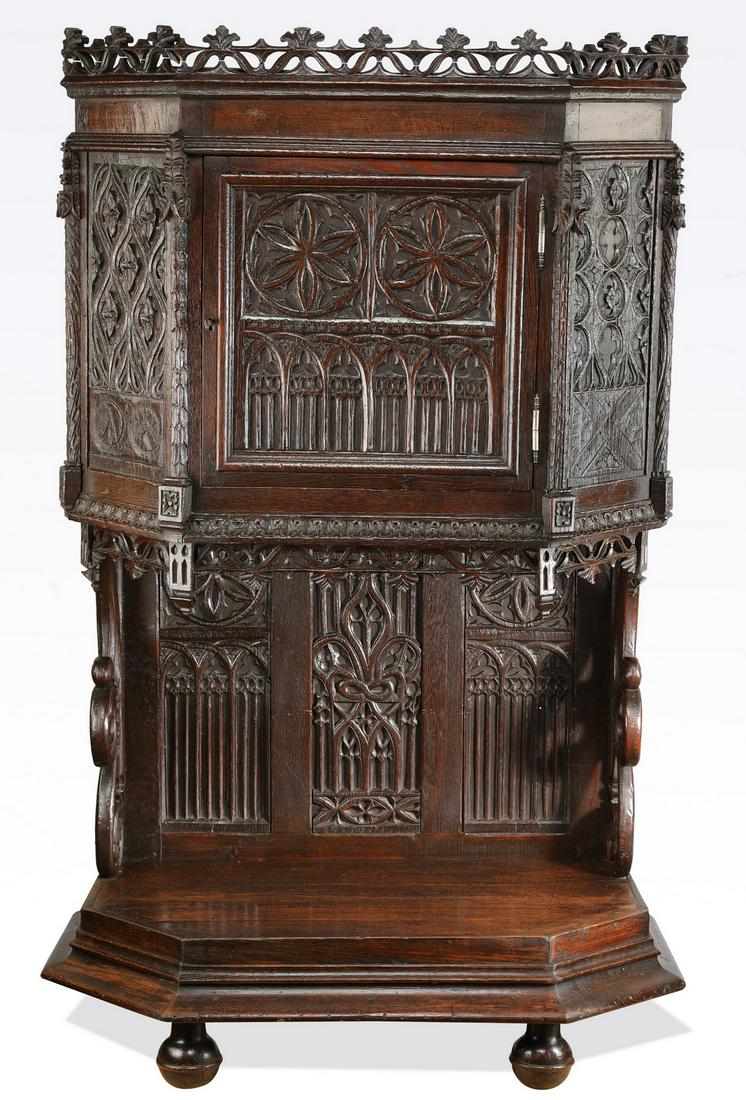 19th c French Gothic Revival oak court cupboard: French Gothic Revival oak court cupboard, 19th century, the five-sided cabinet topped by a pierce carved gallery, above a central door decorated with relief carved rondels and arches, opening to a cri