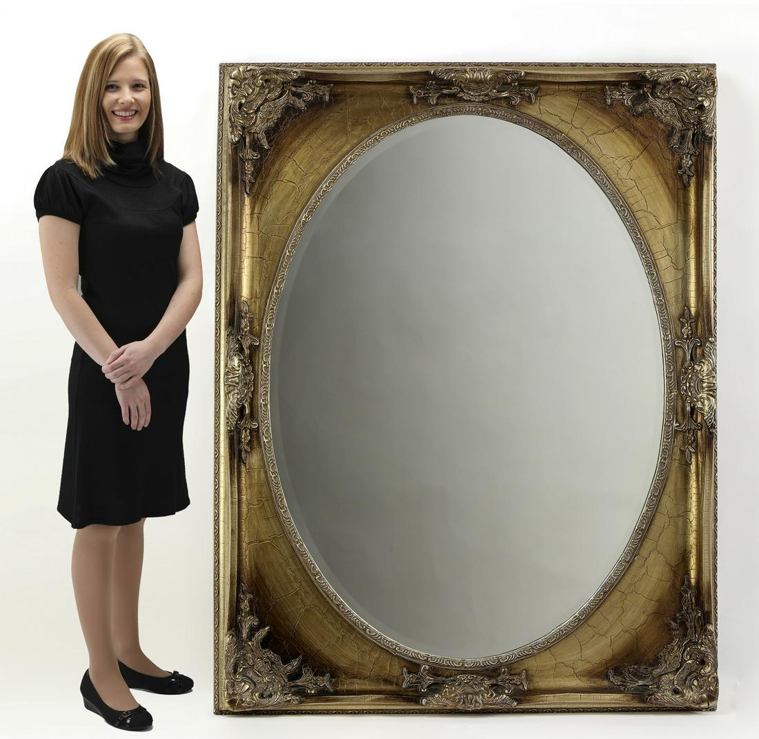 Carved and antiqued gilt-decorated wall mirror: Oversized carved and antiqued gilt-decorated wall mirror, having an oval beveled glass surrounded by a rectangular frame carved with acanthus; mirror 47"h x 34.5"w; overall size with frame 56.25"h x 4
