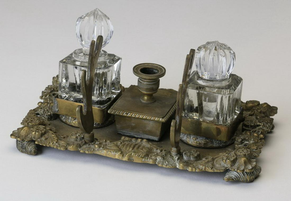 19th c. Continental bronze and crystal inkwell: Late 19th century Continental bronze and cut crystal encrier, with two cut crystal lidded inkwells flanking a pen holder, raised on a rectangular base with decorated rim, 4"h x 7.5"w x 4"d.