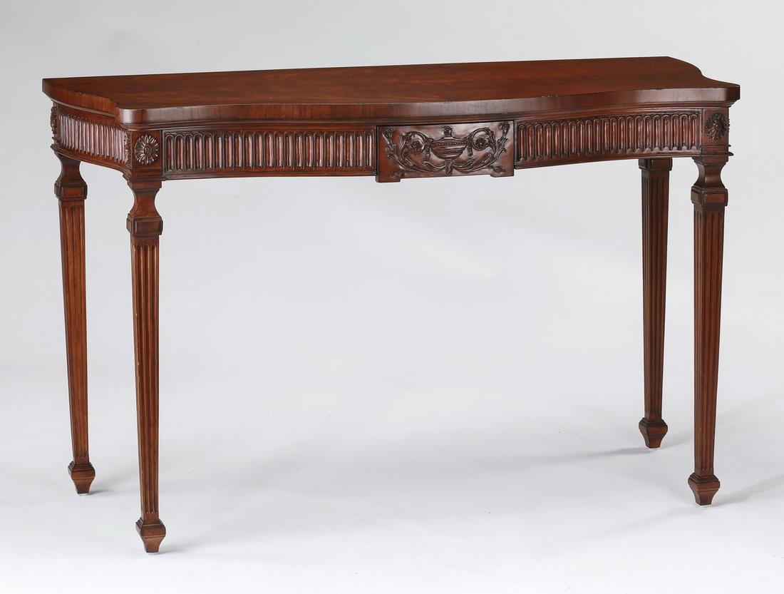 Schumacher serpentine mahogany console table: Serpentine mahogany console table by Schumacher, having a shaped top above a wide fluted apron centering a single drawer carved with an urn and acanthus scrollwork, the whole rising on tapering square