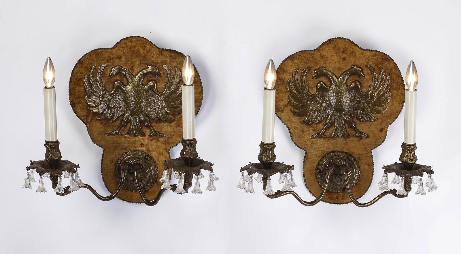 (2) Early 20th c. double-headed eagle sconces: Pair of early 20th century double-headed eagle sconces, executed in brass, velvet, bronze, and crystal, each have a brass double-headed eagle applique on a caramel velvet covered shield back rising ov