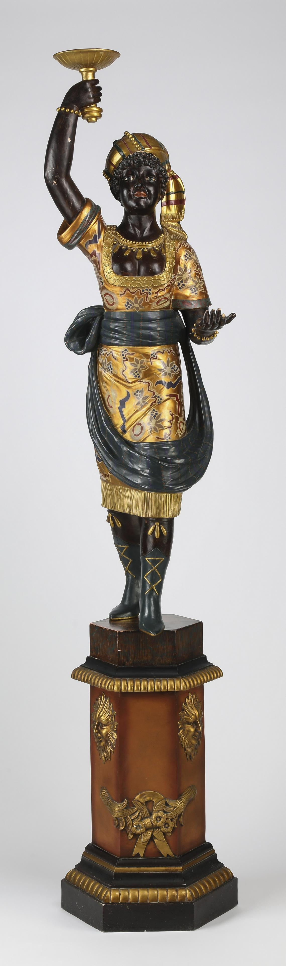 Carved and paint decorated Nubian maiden: Carved and paint decorated Nubian maiden, early 20th century, having a torch held aloft by a standing female figure in exotic turban and fringed dress cinched with a scarf and shod in boots, the whole