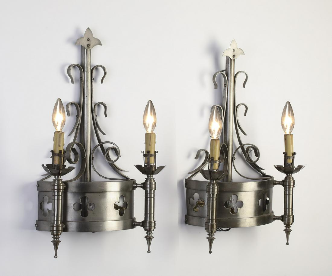 (2) 19th c. French Gothic Revival iron sconces: Pair of French Gothic Revival two-light polished iron sconces, late 19th century, each having a fleur de lis finial over scrolling iron work, a quatrefoil pierced ring, and two torches, 24"h x 12"w x 