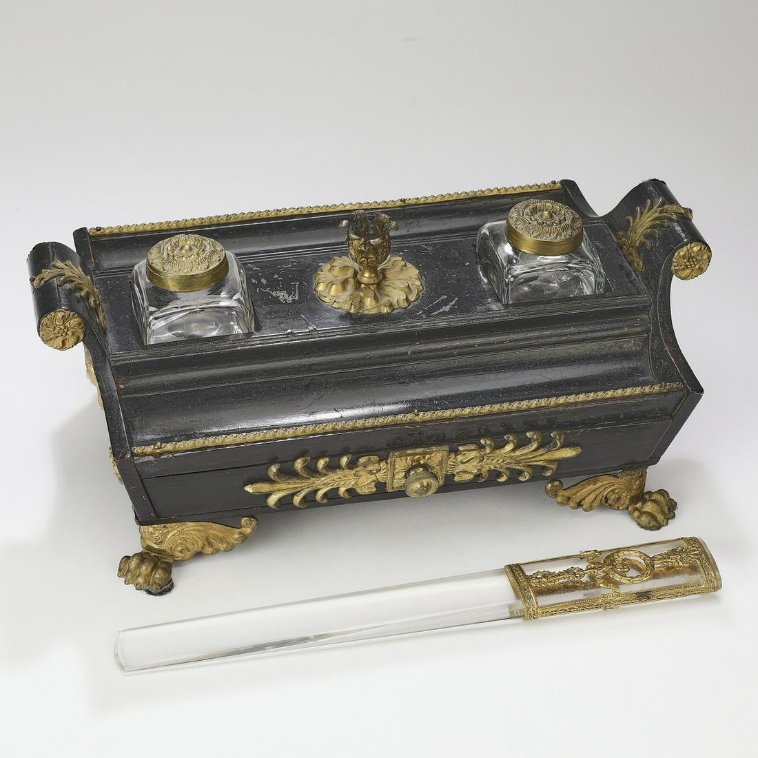 Empire lacquer, brass, and crystal desk set, c. 1830: Continental Empire lacquer, gilt brass, and crystal desk set, circa 1830, the inkstand of rectangular form, centering a foliate gilt brass candleholder flanked by glass ink bottles, with a pen well to