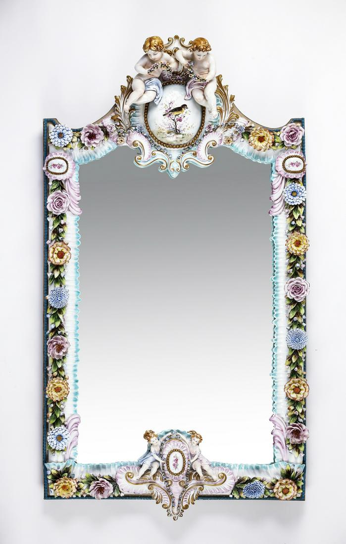 Italian porcelain wall mirror with putti and florals: Italian porcelain wall mirror in the Rococo taste, having a pair of putti holding garlands resting on a cabachon painted with a bird perched on a blossoming tree, the whole framed by rocaille and elab