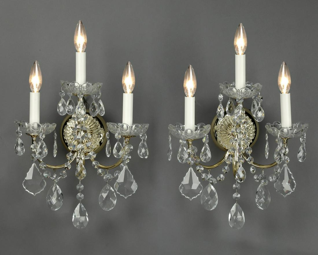 (2) Schonbek crystal 3-light wall sconces, 18"h: Pair of Schonbek crystal 3-light wall sconces, each having a circular brass mount with a cut crystal dome top, issuing three 'U' shaped arms hung with crystal swags and pendants, each terminating in c