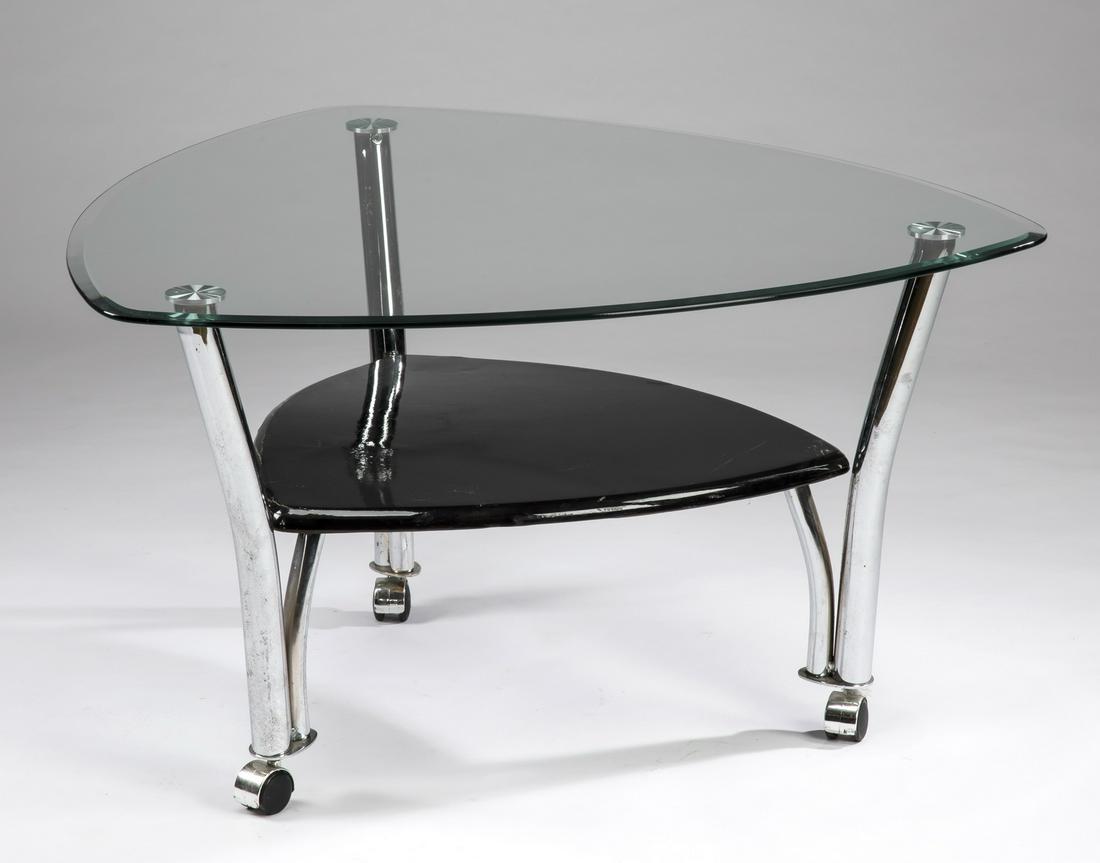Contemporary glass and chrome side table: Glass and chrome side table, in the Moderne style, the triangular glass top over an ebonized wood shelf, with the supports joining the three legs raised on casters, 20.5"h x 36"w.