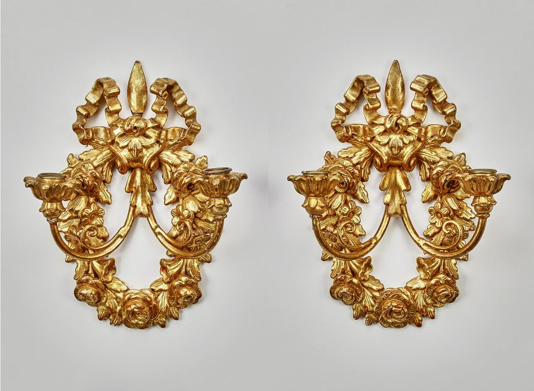 (2) Italian giltwood candle sconces: Pair of Italian giltwood candle sconces in the Neoclassical taste, mid 20th century, each having a carved bow finial issuing a floral swag and two scrolling arms terminating to foliate candle cups, 12