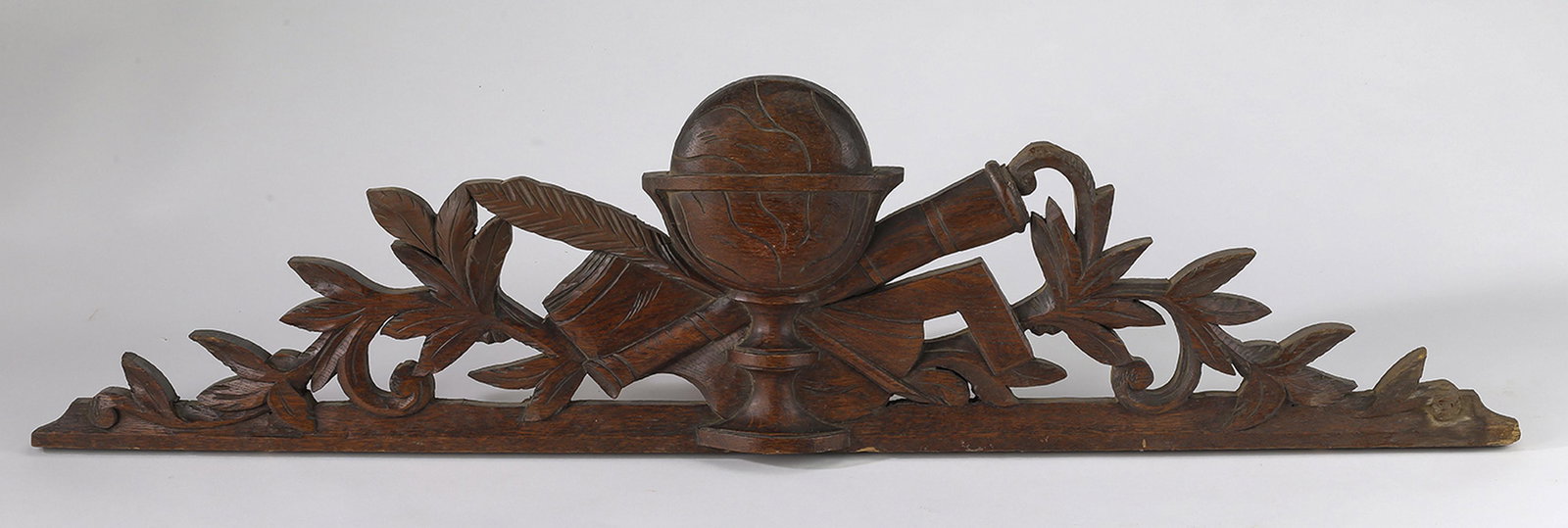19th c. Continental relief carved walnut pediment: 19th century Continental pierced and relief carved walnut pediment, having a globe crossed with a monocular and quill pen, flanked by naturalistic carvings, 10"h x 39.5"w x 2"d.