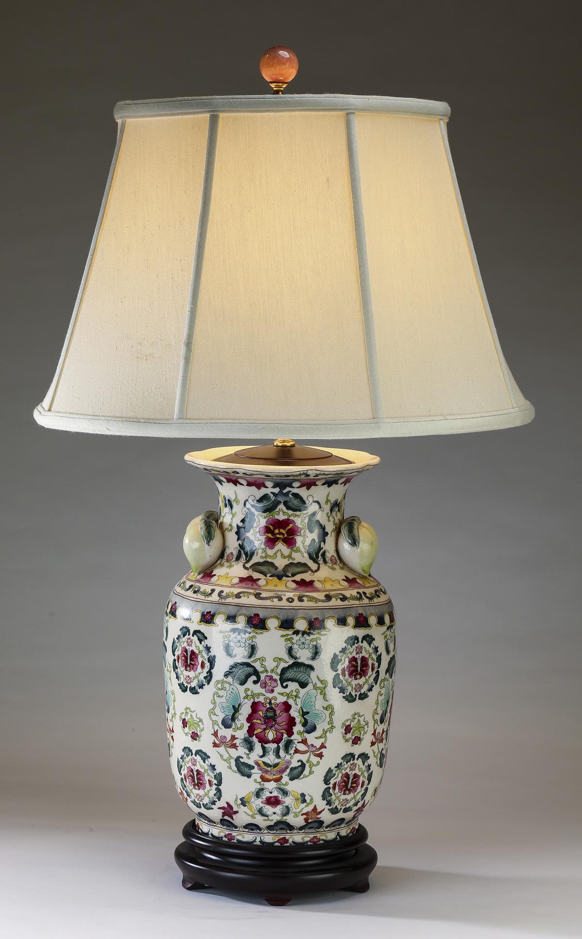 Chinese hand painted porcelain table lamp: Chinese porcelain table lamp, having an ivory shade surmounting the porcelain vasiform standard, accented with double peach handles and painted with lotus scrollwork and butterflies, the whole rising
