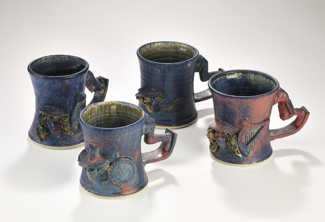 (4) Signed Michael Kennedy Ceramics art pottery mugs: Set of (4) signed Michael Kennedy Ceramics art pottery mugs, of tapered form with drip-glaze interiors, in hues of cobalt and dusty rose, accented with sculpted musician medallions, flanked by handles