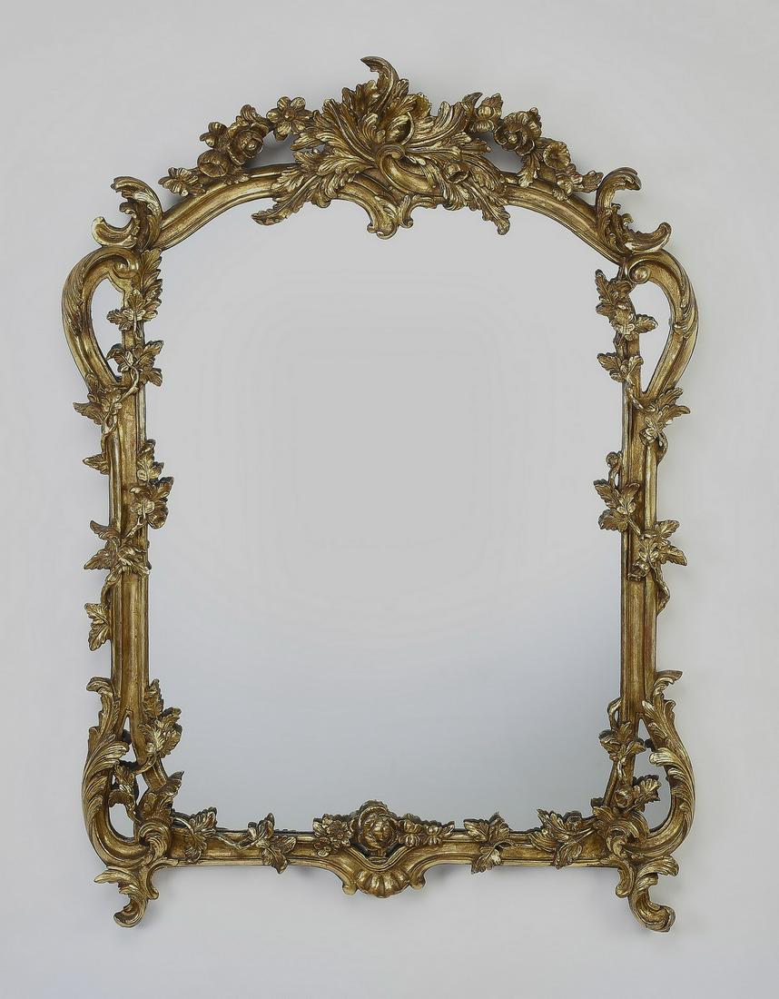 Giltwood wall mirror in the Rococo taste, 44"h: Giltwood wall mirror in the Rococo taste, having a pierced and carved foliate crest with swags surmounting an arched mirror framed with 'C' scrolls and twining floral vines, the whole terminating to a