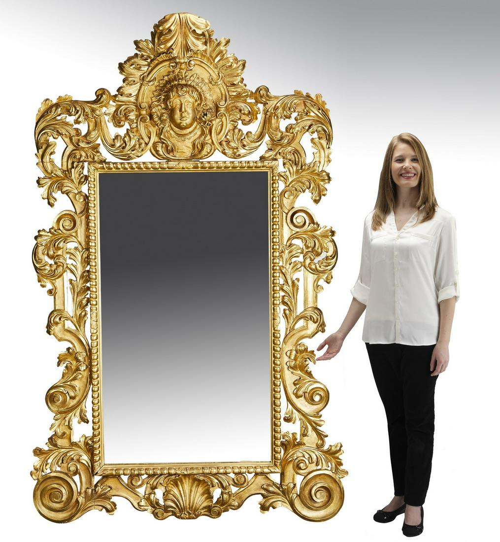 Monumental giltwood mirror in the Baroque style: Monumental giltwood mirror in the Baroque style, the crest centering a finger carved acanthus leaf over a putto mask, flanked by scrolling pierce carved acanthus, extending to envelope a rectangular m