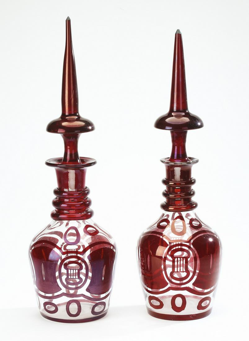 (2) Monumental ruby flash decanters, ca 1900: Near pair of monumental ruby flash decanters, circa 1900, each having a spear form finial surmounting a mushroom form stopper, above flattened rims and cylinder necks with three graduated bands, issui