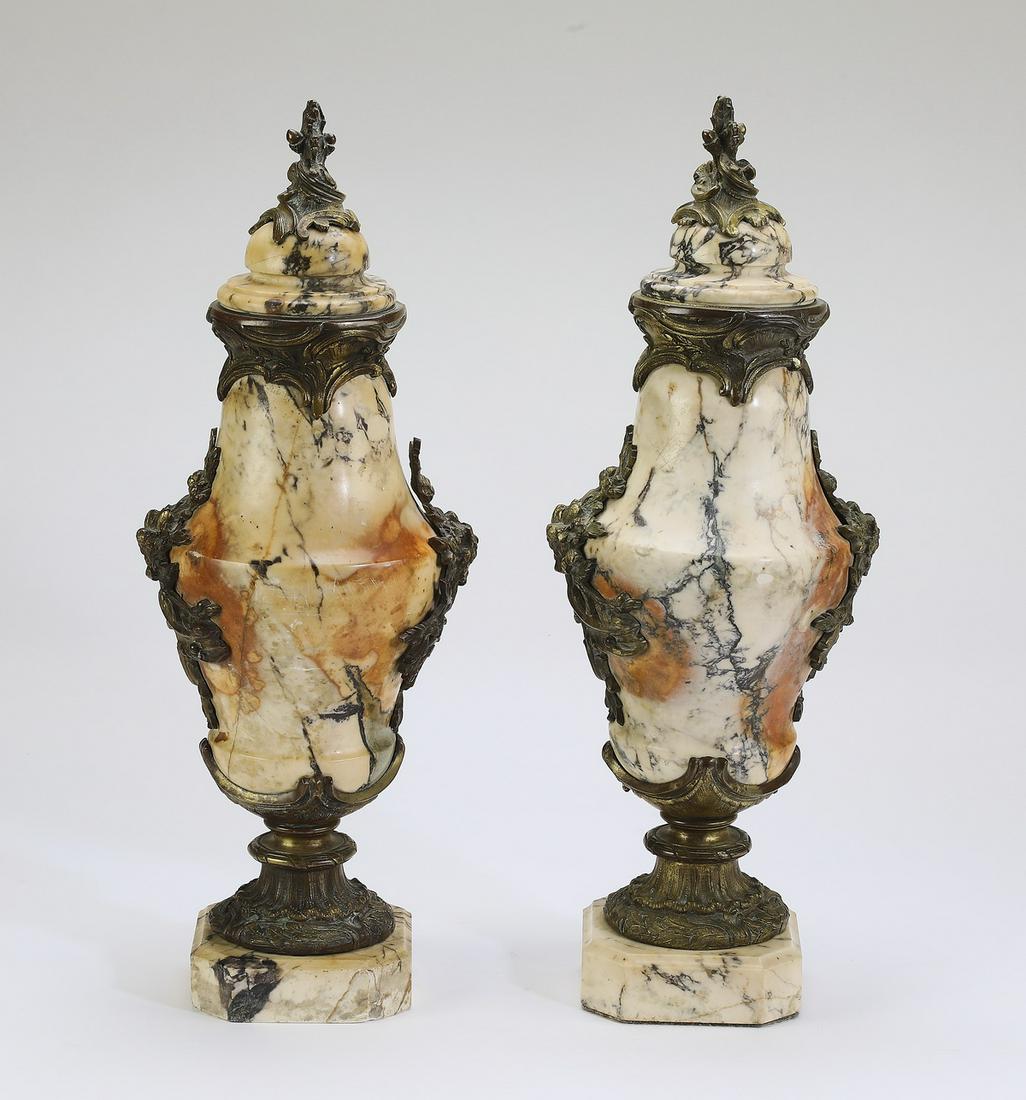 (2) 19th c. French bronze and marble cassolettes: Pair of 19th century French bronze mounted cream and russet breccia marble cassolettes in the Rococo taste, each having a foliate finial rising on the attached cover, surmounting the vasiform body mou