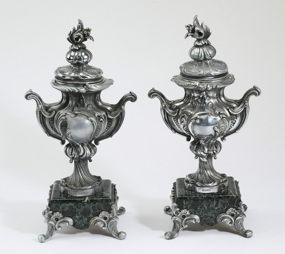 (2) French Rococo Revival style covered urns: Pair of French Rococo Revival style covered urns, executed in silver patinated spelter and marble, each having a lid with a rocaille finial above an urn form body with scrolled handles and cabochon de