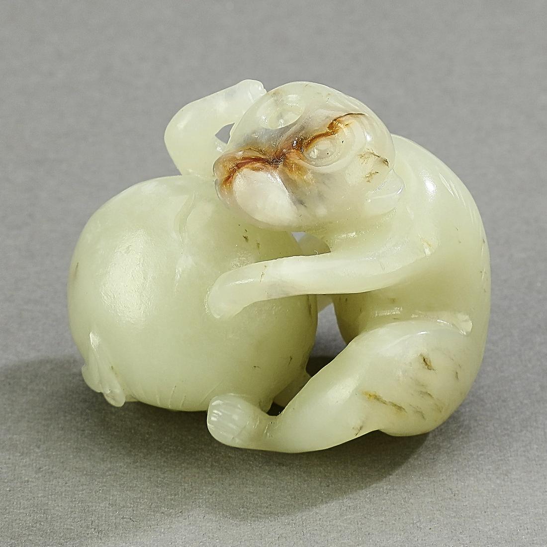 Chinese jade carving of a monkey and peach: Chinese jade carving, executed in celadon jade with russet inclusions, depicting a seated monkey holding a peach, 1.5"h x 2"w x 1.25"d.
