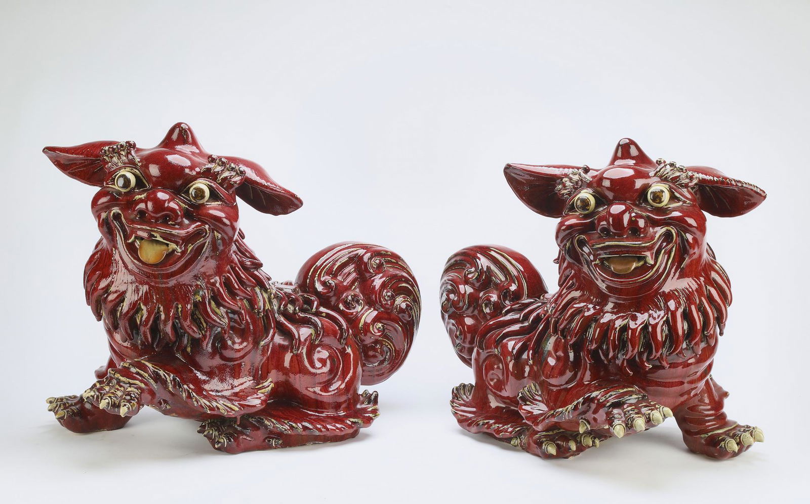 (2) Maitland-Smith glazed terracotta Fu lions: Pair of Maitland-Smith terracotta Fu lions, each having sang de boeuf glaze and playful expressions, 18.5"h x 13"w x 21"l.