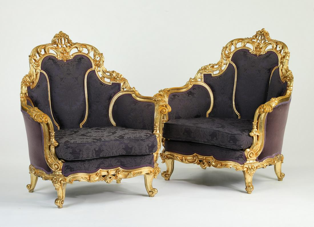 (2) Extravagant Italian carved giltwood bergeres: Pair of extravagant Italian giltwood bergeres, each having a pierce carved crest leading to curved arms, centering the damask back and seat, the exterior upholstered in velvet, terminating to cabriole
