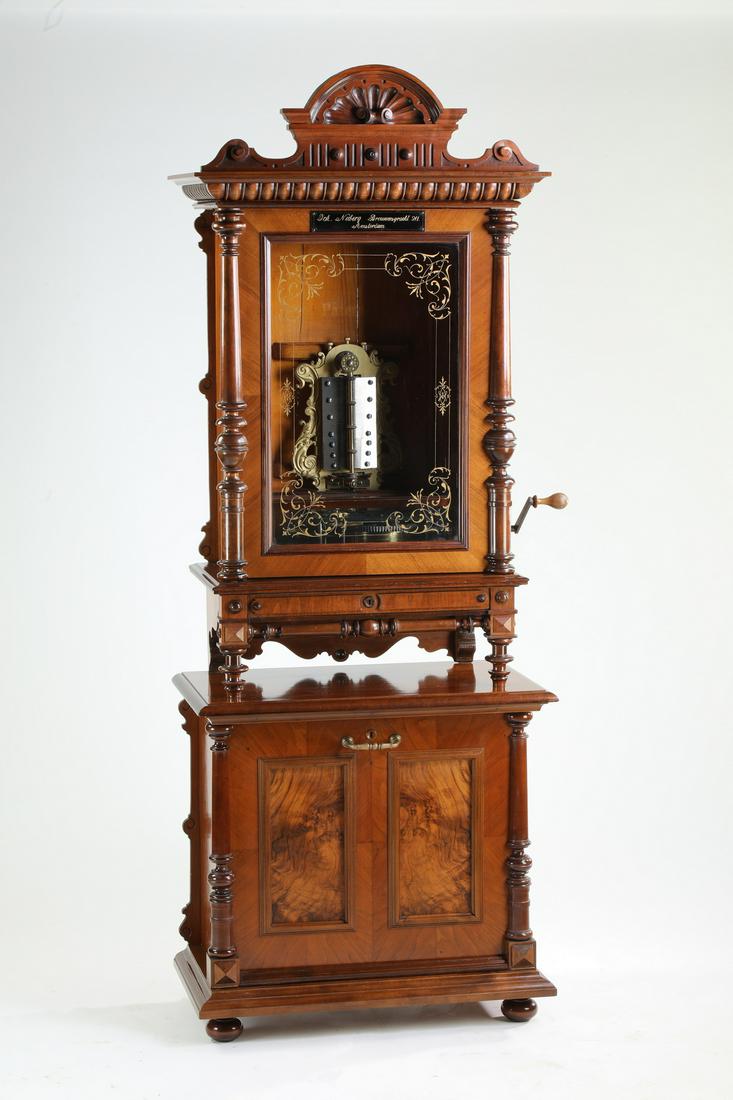 (11 pcs) German upright coin-op music-box w/ disks: German upright coin-op music-box on stand, circa 1890, having a Renaissance Revival walnut case with an arched crest above a pediment with dentil and gadrooned molding, surmounting a glazed door with 