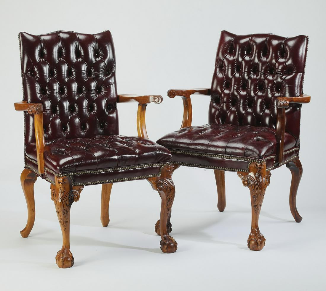 (2) Leather upholstered Chippendale style armchairs: Pair of leather upholstered Chippendale style armchairs, executed in hardwood and oxblood leather with nailhead trim, having tufted tablet backs flowing into arms with scrolling hand rests, flanking c