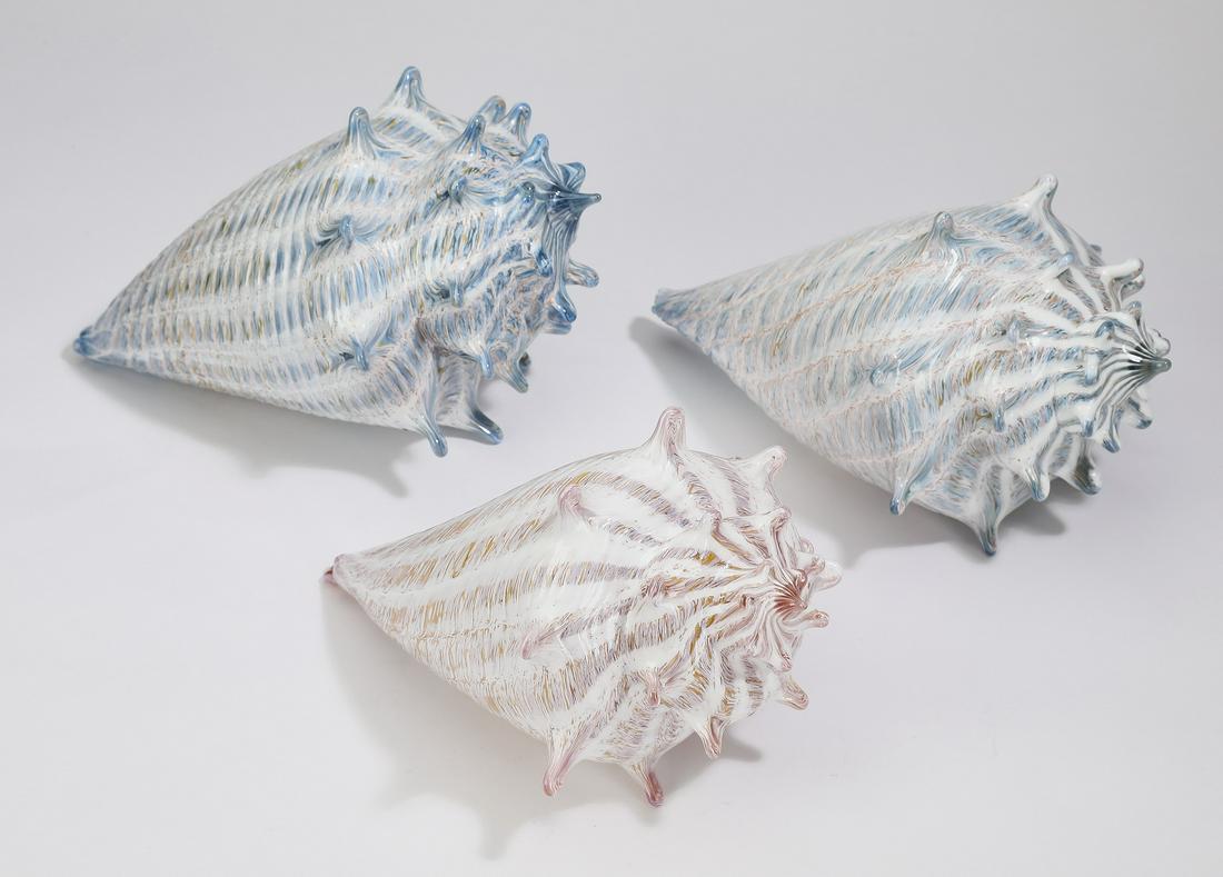 (3) Art glass conch shells by Treg Silkwood: Three art glass conch shells, by Treg Silkwood of Silkwood Studios, one with slate blue, one with teal, and one with a pink zanfirico interior, largest 4"h x 8.5"l x 6"w.
