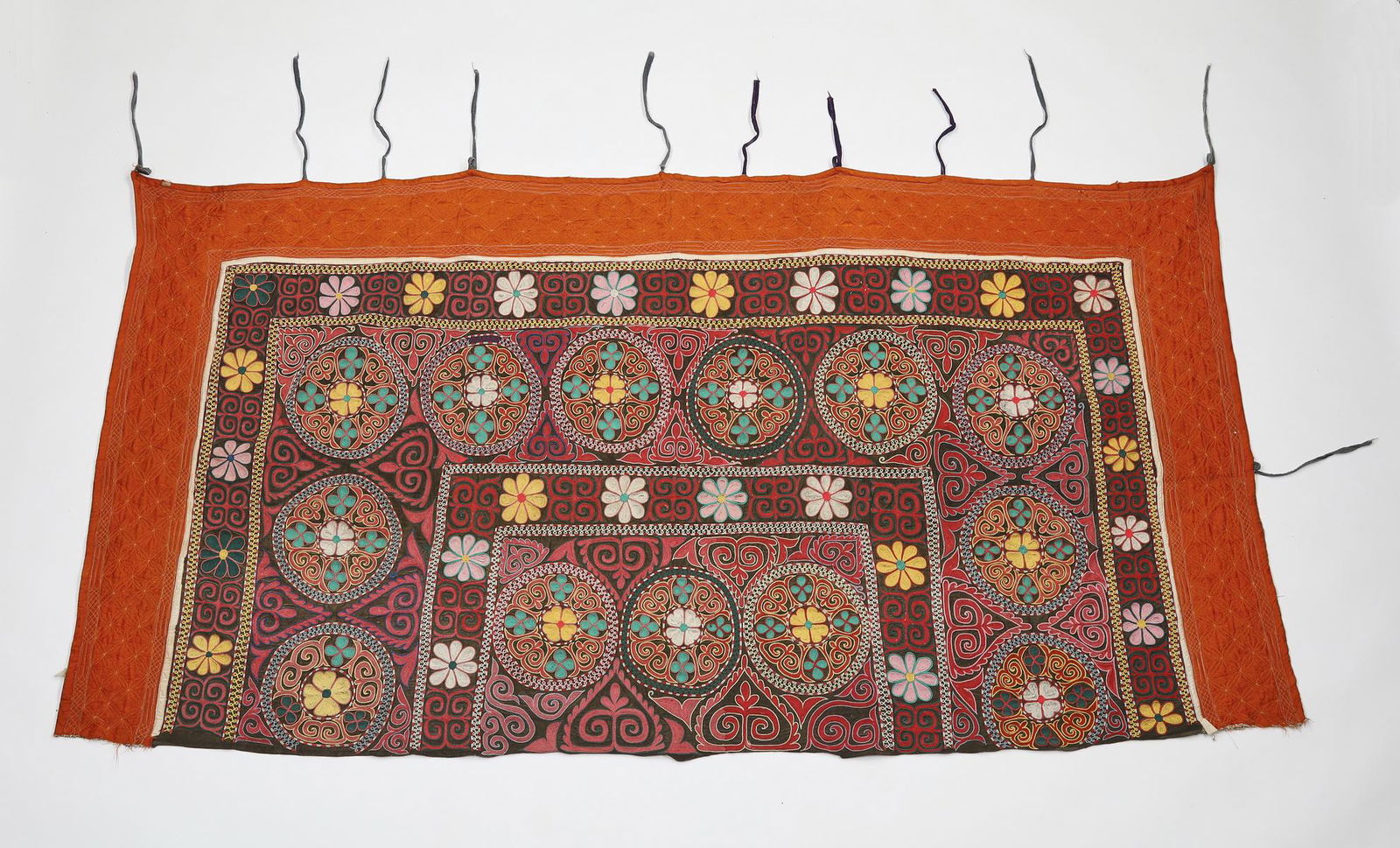 Kazakh tuskiiz hand embroidered suzani 'headboard': Kazakh tuskiiz or fabric 'headboard,' 20th century, executed in cotton and silk, having hand embroidered repeating roundels of chain stitch in cream, teal, crimson, and pale yellow on a brown ground w