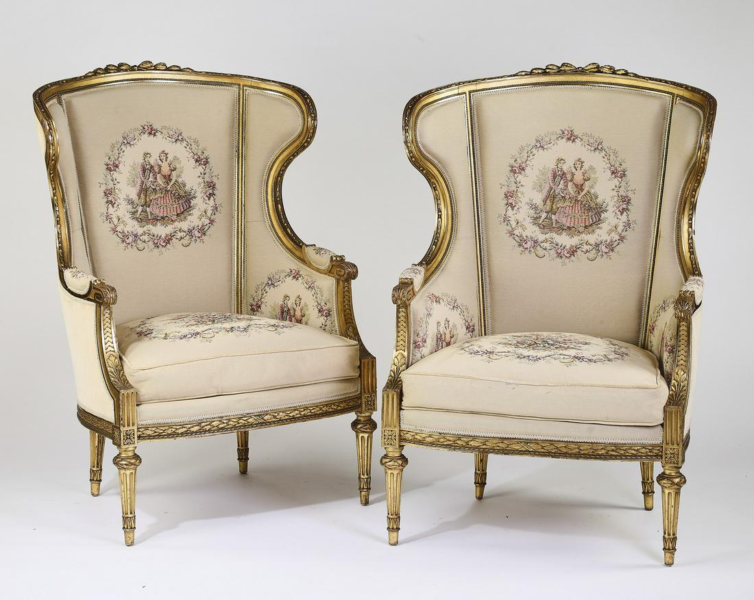 (2) Louis XVI style gilt wood wing chairs in tapestry: Pair of Louis XVI style wing chairs, each having a gilt decorated crest sloping to the padded arms, centering the back and drop-in seat cushions upholstered in tapestry fabric depicting courting coupl