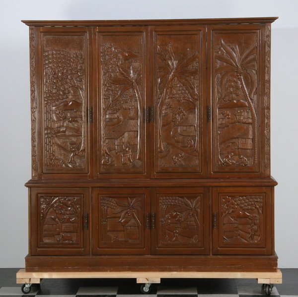 Intricately relief carved teak wall unit: Carved teak wall unit with upper bi-fold doors opening to shelved storage, over a four door base cabinet with interior drawers and shelves, the door panels relief carved with tropical scenes, 74.5"h x
