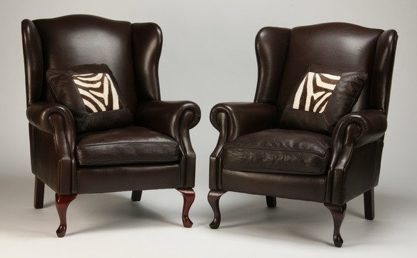 (2) wingback chairs upholstered in leather: Pair of English wingback chairs upholstered in dark brown leather, each with a throw pillow accented in zebra skin hide, 43"h x 35"w x 32"d.