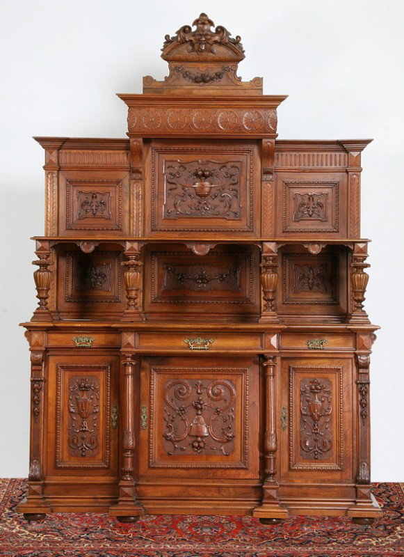 19th c. French walnut buffet: Late 19th century French carved walnut buffet, the crest with Northwind mask, the upper cabinet with foliate carved panels and display shelf raised on baluster form supports, over a three drawer, thre