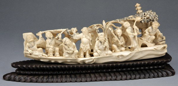 19th c. carved Asian ivory tusk: Finely carved late 19th century Asian ivory tusk depicting figures in a boat crossing the ocean, representing a famous Chinese fable, on fitted hardwood base; ivory 6"h x 14.5"l x 4.5"diam.; carved ba