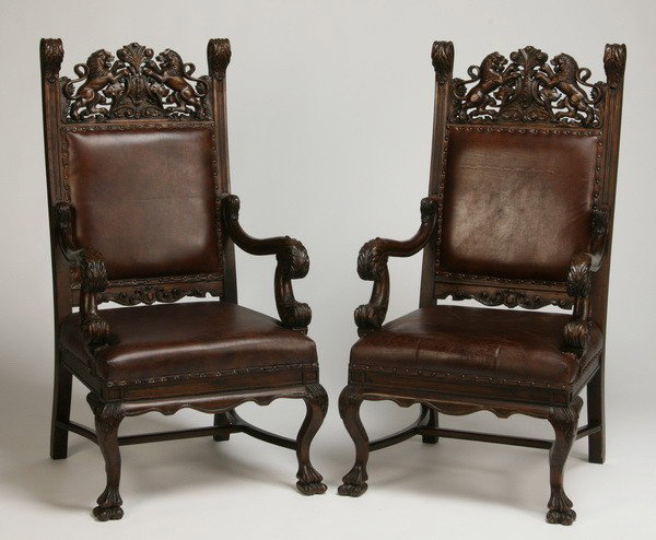 Pair of carved oak arm chairs in leather: Pair of carved quarter sawn oak arm chairs with pierce carved crest flanked by battling lions, the legs terminating in lion's paw feet, upholstered in dark brown leather, 50"h x 28"w x 33"d.