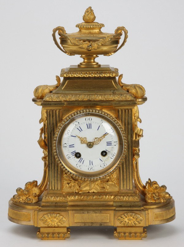 19th c. French dore' bronze clock: Mid 19th century dore' bronze French Empire clock, the porcelain clock face surmounted by a lidded irn and flanked by fluted pilasters, 13"h x 10"w x 5"d.